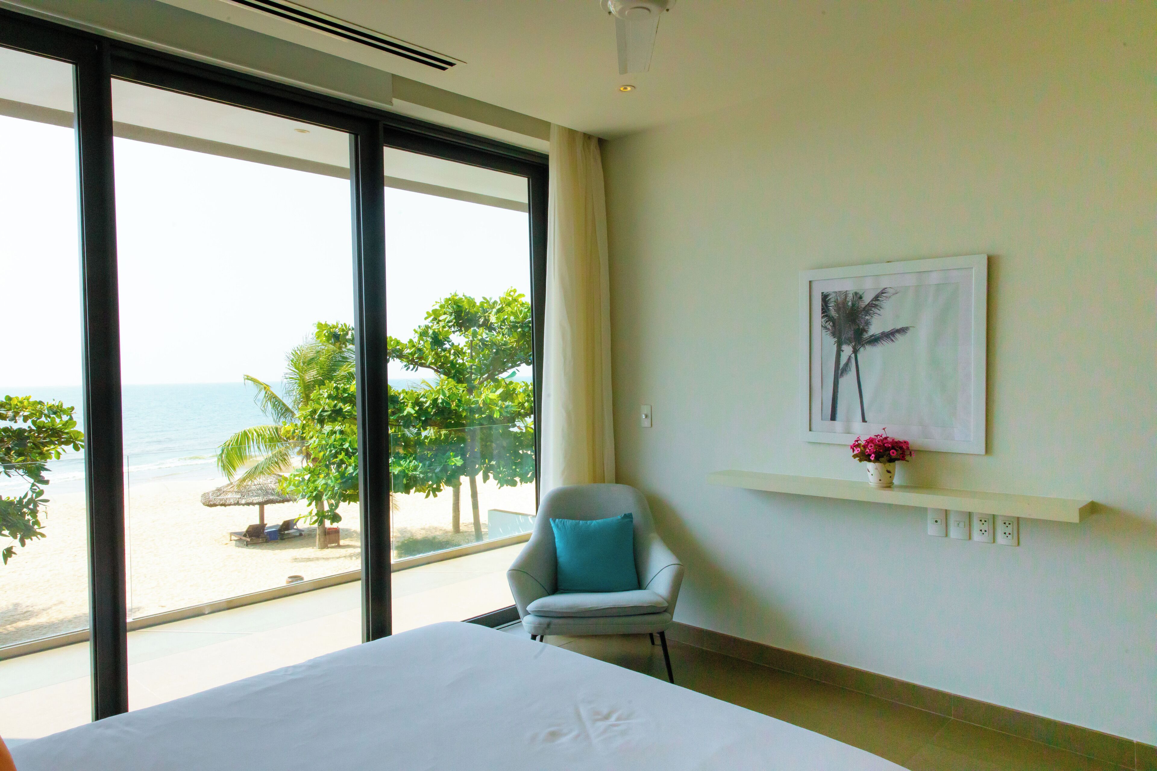 Une chambre d’hôtel dotée d’une grande fenêtre donnant sur la plage et les palmiers.