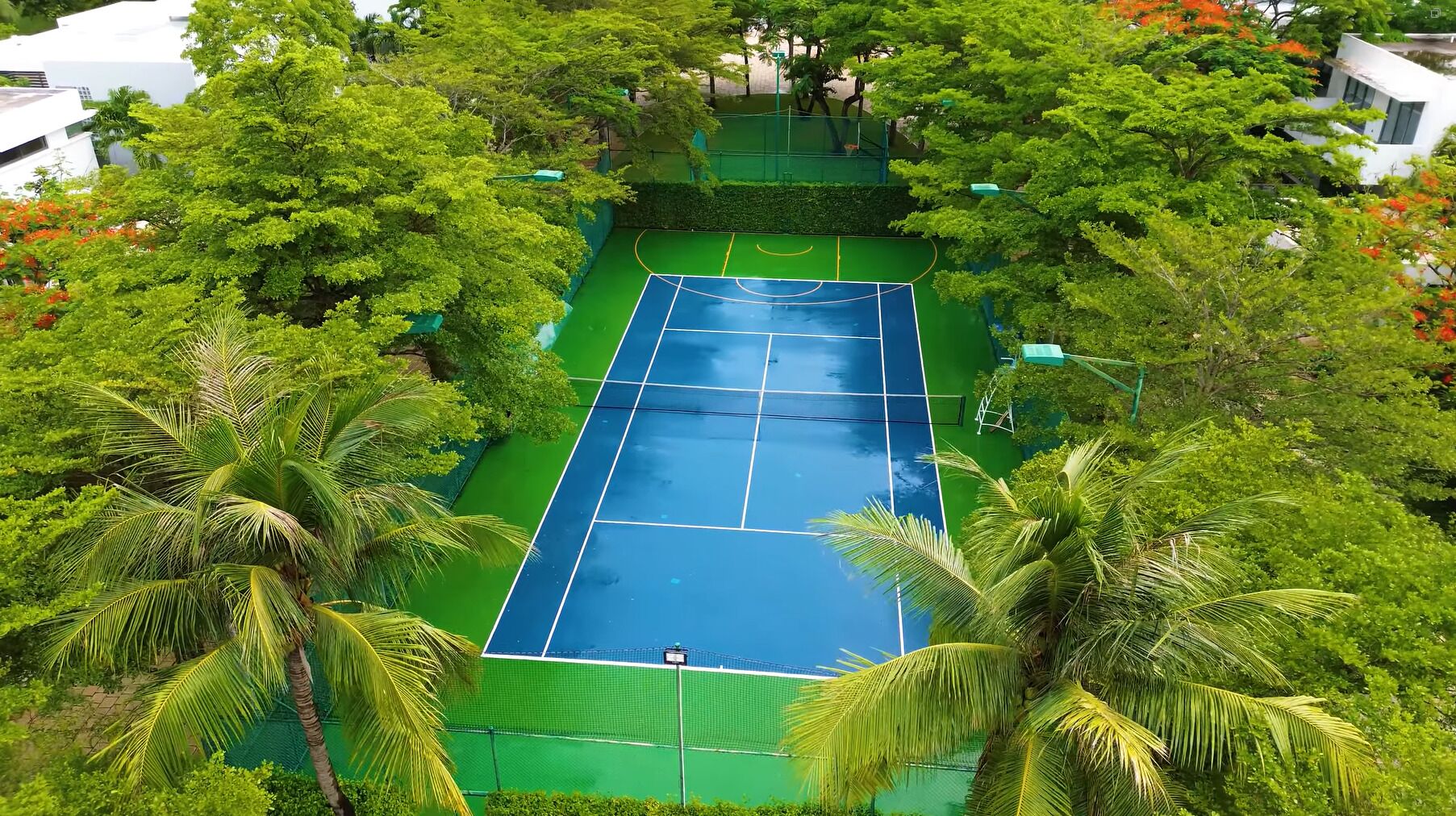 Una vista aèria d'una pista de tennis envoltada de vegetació exuberant i palmeres.