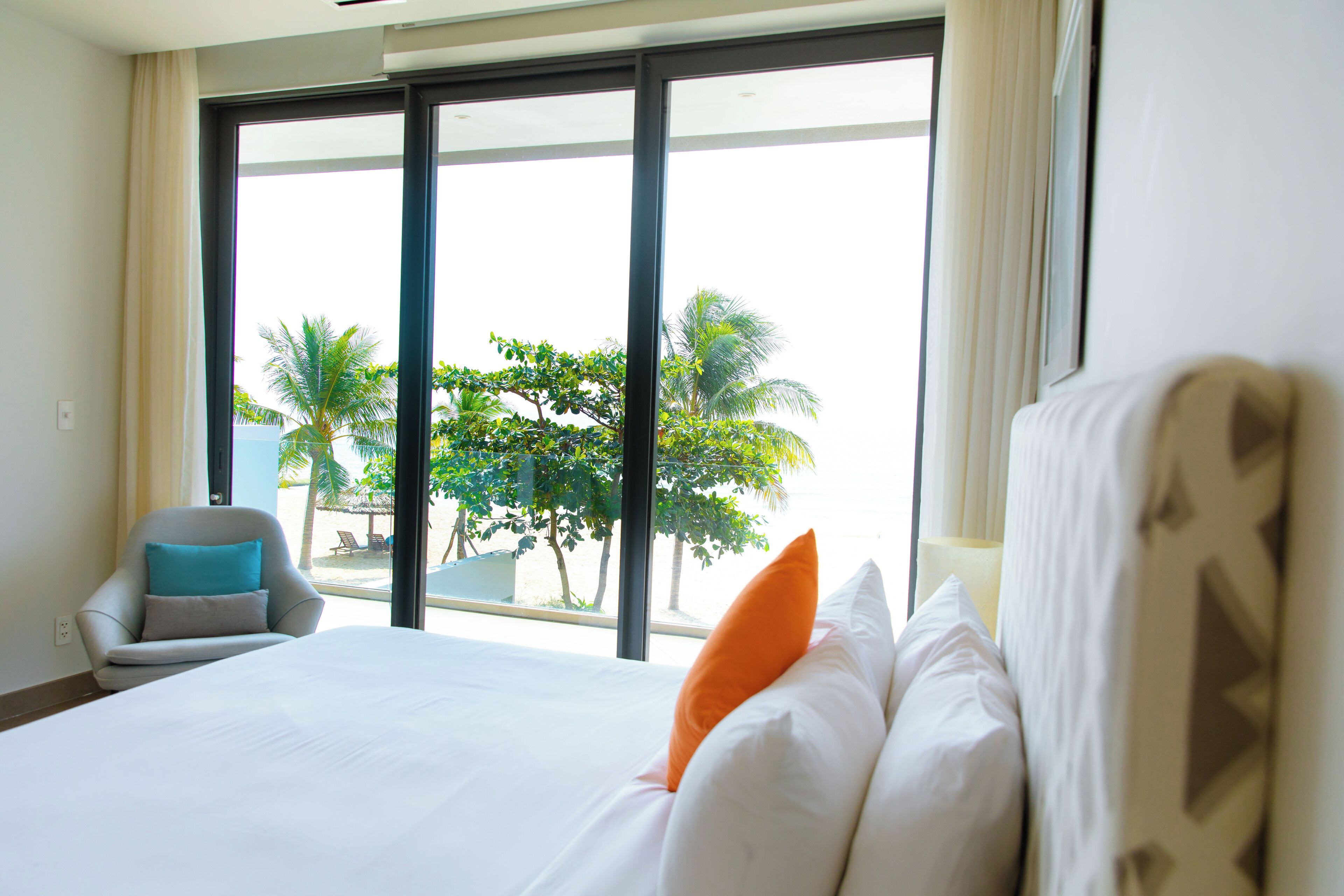 A hotel room with a large bed, a chair, and a view of palm trees through the window.