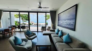 A modern living room with a large window, a ceiling fan, and a view of a pool and beach.