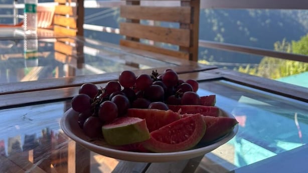 Ein Tisch mit einer Fruchtplatte, einer Flasche und einem Stuhl mit Blick auf die Berge.