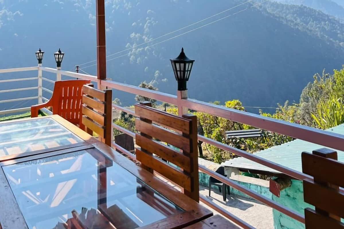 Una terraza de madera con una mesa de vidrio y bancos, con vistas a un paisaje montañoso.
