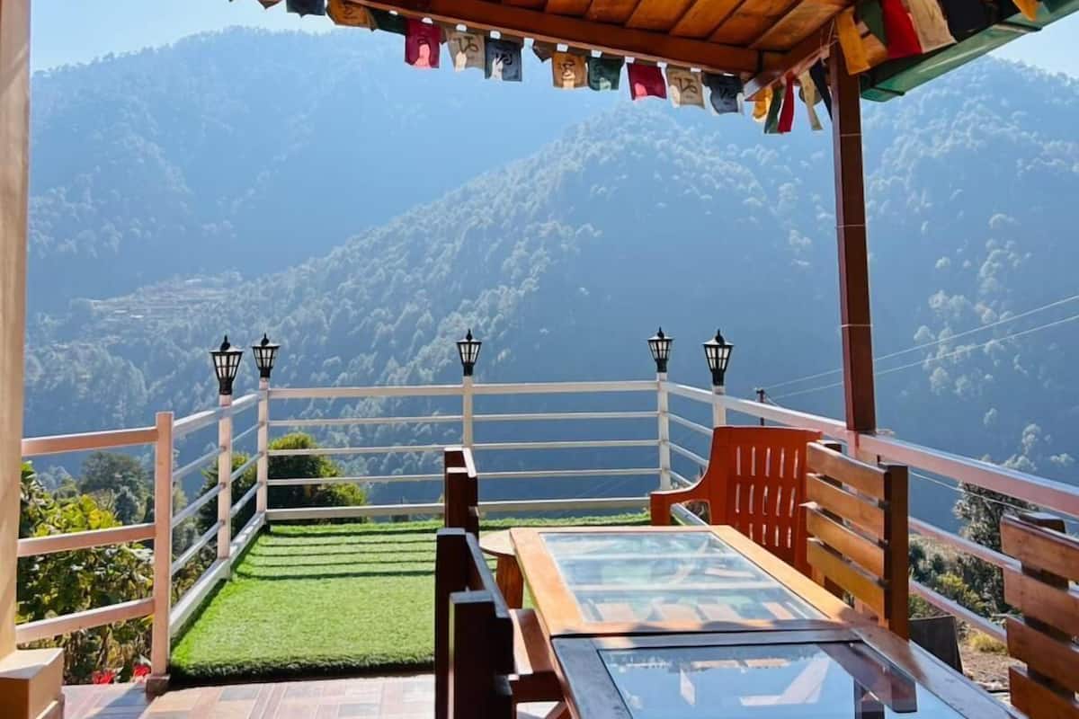 Una pérgola de madera con una mesa y bancos de vidrio, con vistas a un paisaje montañoso.