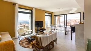 Een ruime woonkamer met een televisie, zitplaatsen en een balkon met uitzicht.