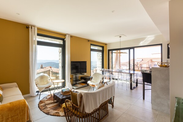 A spacious living area with a TV, seating, and a balcony with a view.