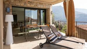 Een balkon met een stenen muur, een tafel met stoelen en een lounge stoel met kussen.