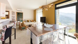 Een moderne woonkamer met een eethoek, een zithoek, een televisie en een groot raam met uitzicht op de bergen.