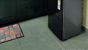 Une cuisine compacte avec des meubles de couleur vert foncé, un pare-feu en carreaux, un petit réfrigérateur, une bouilloire et un ventilateur.