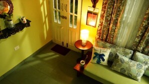 Une pièce avec un canapé vert, une petite table avec une lampe et une porte avec des rideaux.