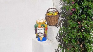 A corner of a building with a white wall, a bamboo fence, a small garden with a potted plant, and a decorative sculpture of a king. - Etna Docet, Nicolosi center (Nicolosi)