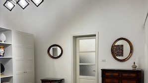 A room with a bed, a wooden dresser, a table with chairs, a shelf with decorative items, and a door with frosted glass. - Etna Docet, Nicolosi center (Nicolosi)