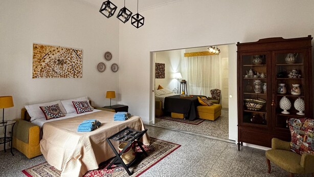 A spacious living room with a large bed, a wooden cabinet with glass doors, and a red patterned rug. - Etna Docet, Nicolosi center (Nicolosi)