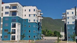 A multi-story residential building with balconies, a clear view of a mountain, and a well-maintained lawn area. - Simpson's Little Gem 2 (Kingston)