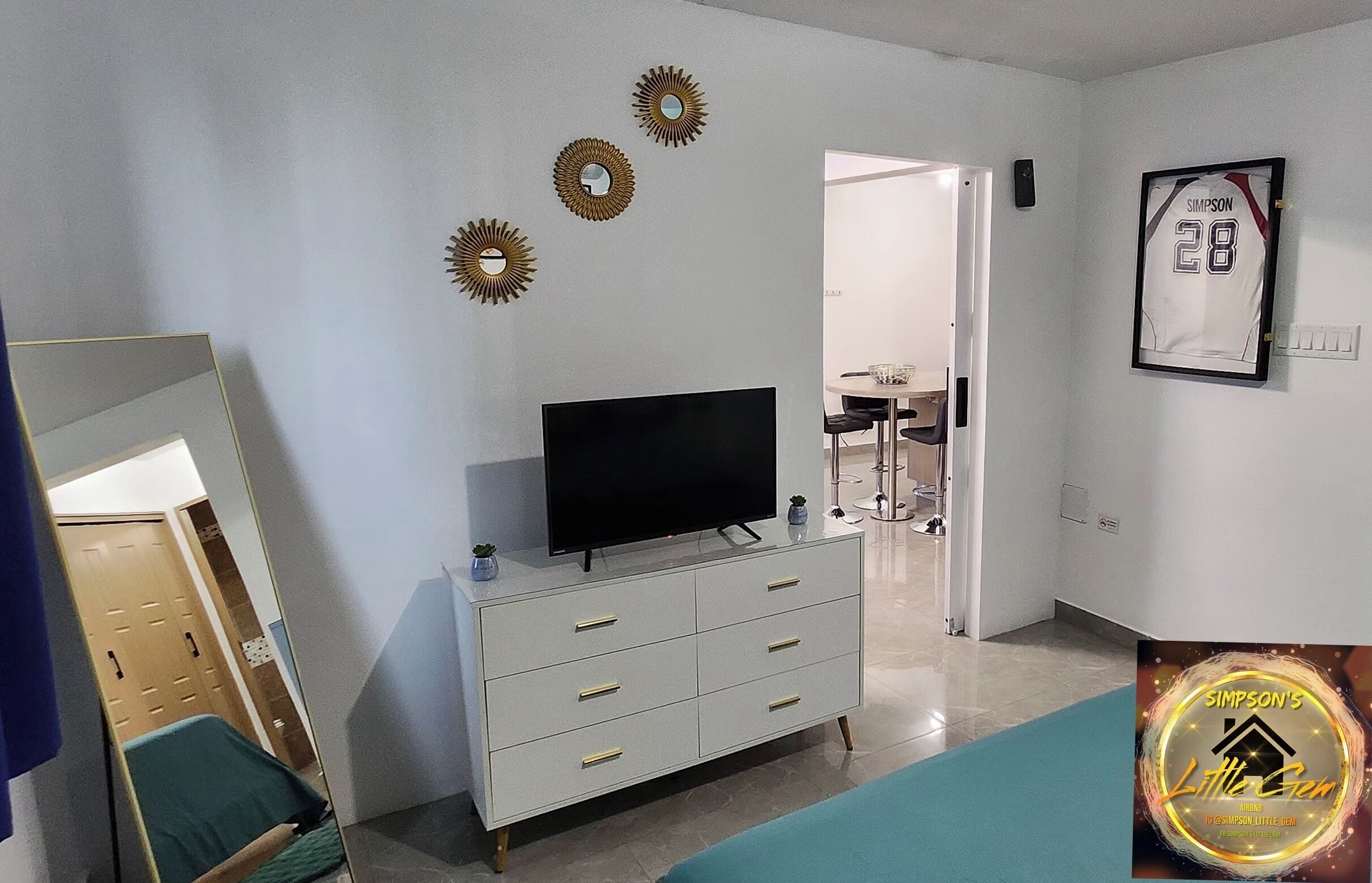Un salon moderne avec un téléviseur à écran plat posé sur un meuble blanc, des miroirs décoratifs au mur et un maillot de sport encadré.