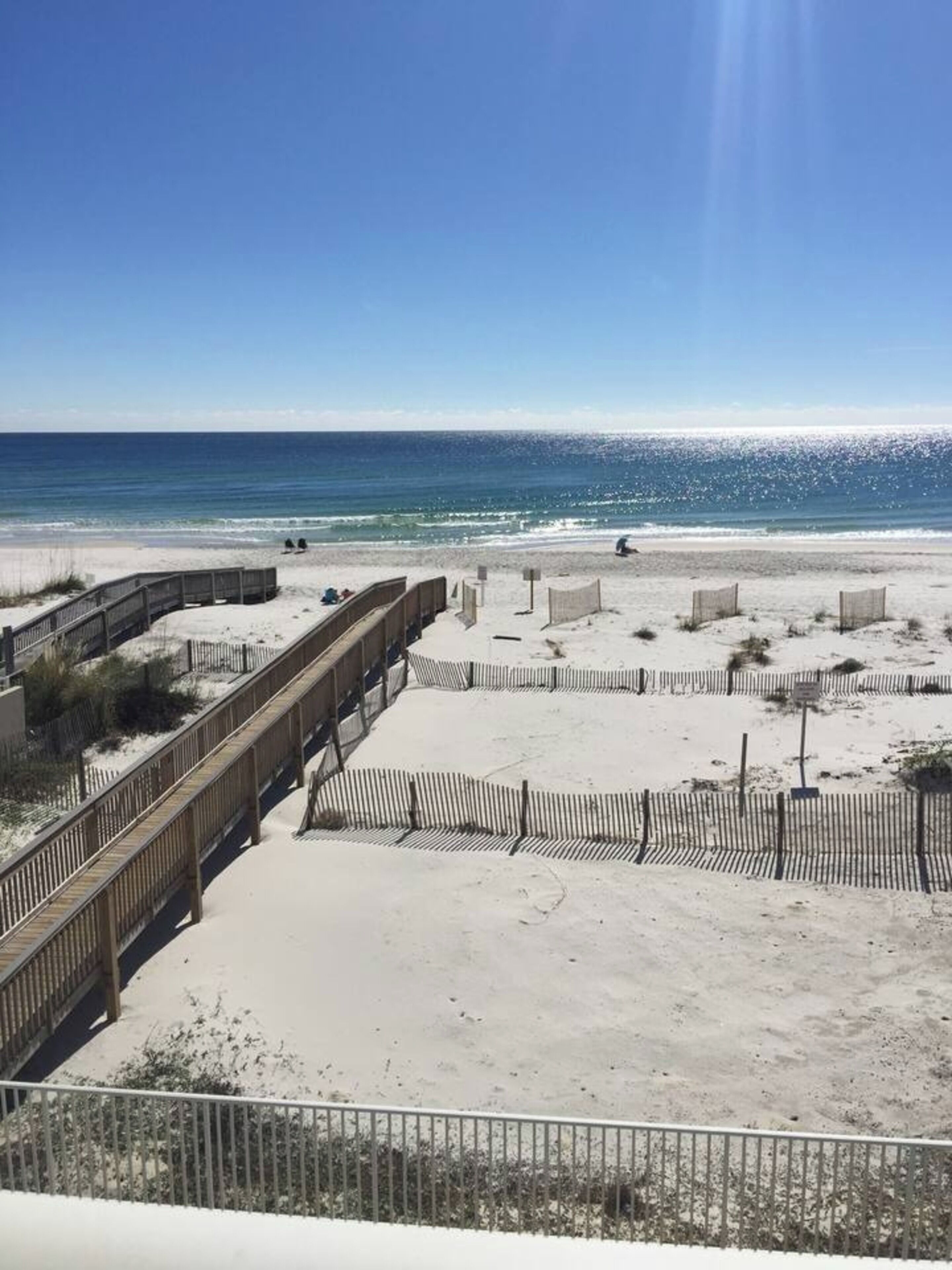 Een strand met een houten vlinderpad, zandgebieden en een helder uitzicht op de zee.