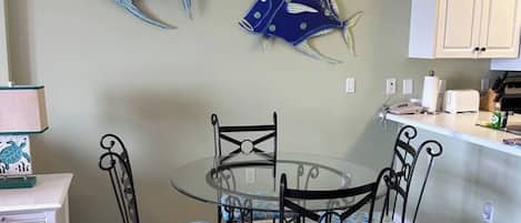 A dining area with a glass table and metal chairs, a chandelier, and decorative fish wall art.