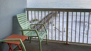 Un balcon avec deux chaises vertes et une petite table, donnant sur une plage enneigée avec une jetée.
