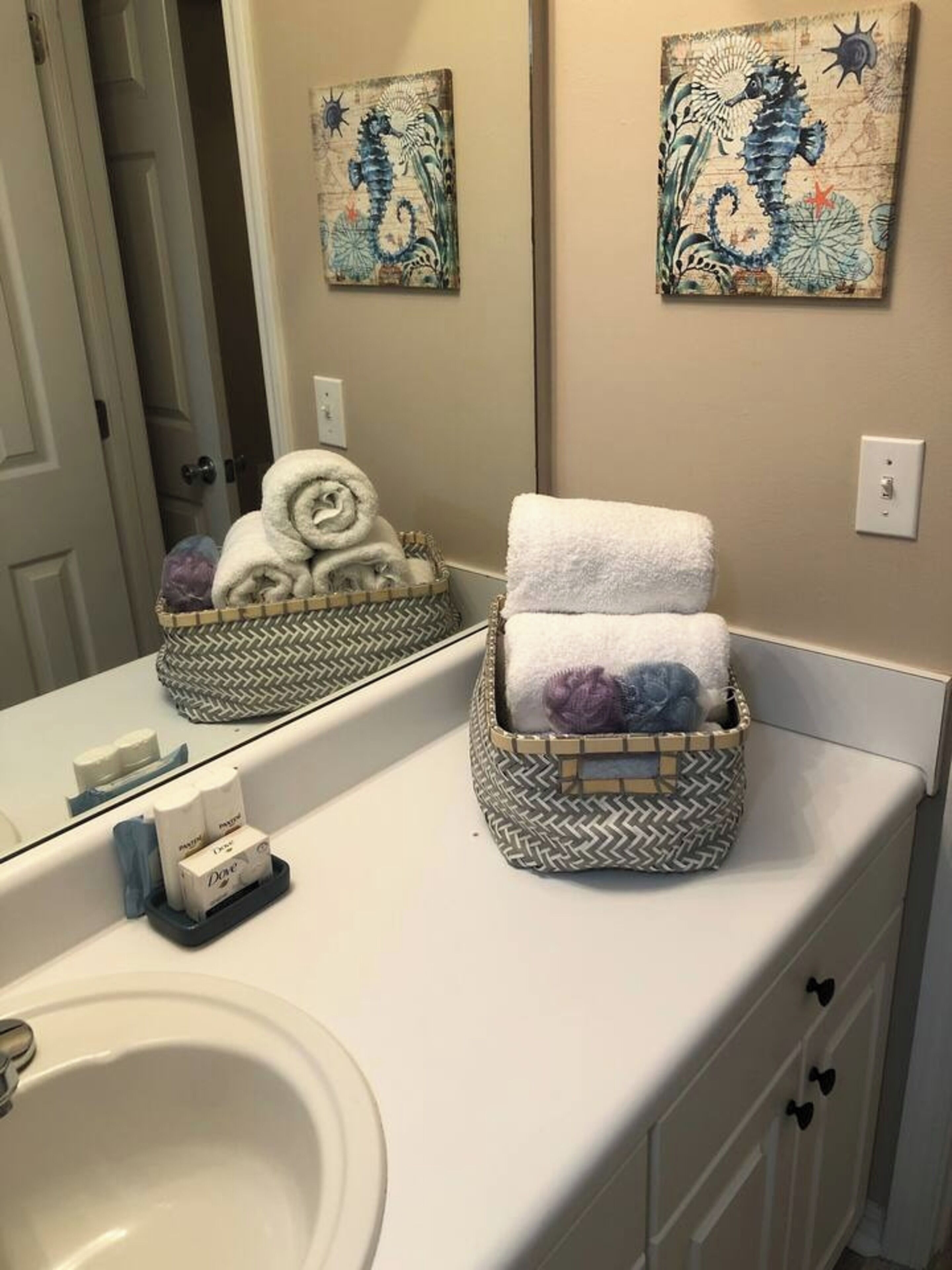 Une salle de bain avec un lavabo blanc, deux paniers à serviettes posés sur le comptoir et deux tableaux accrochés au mur.