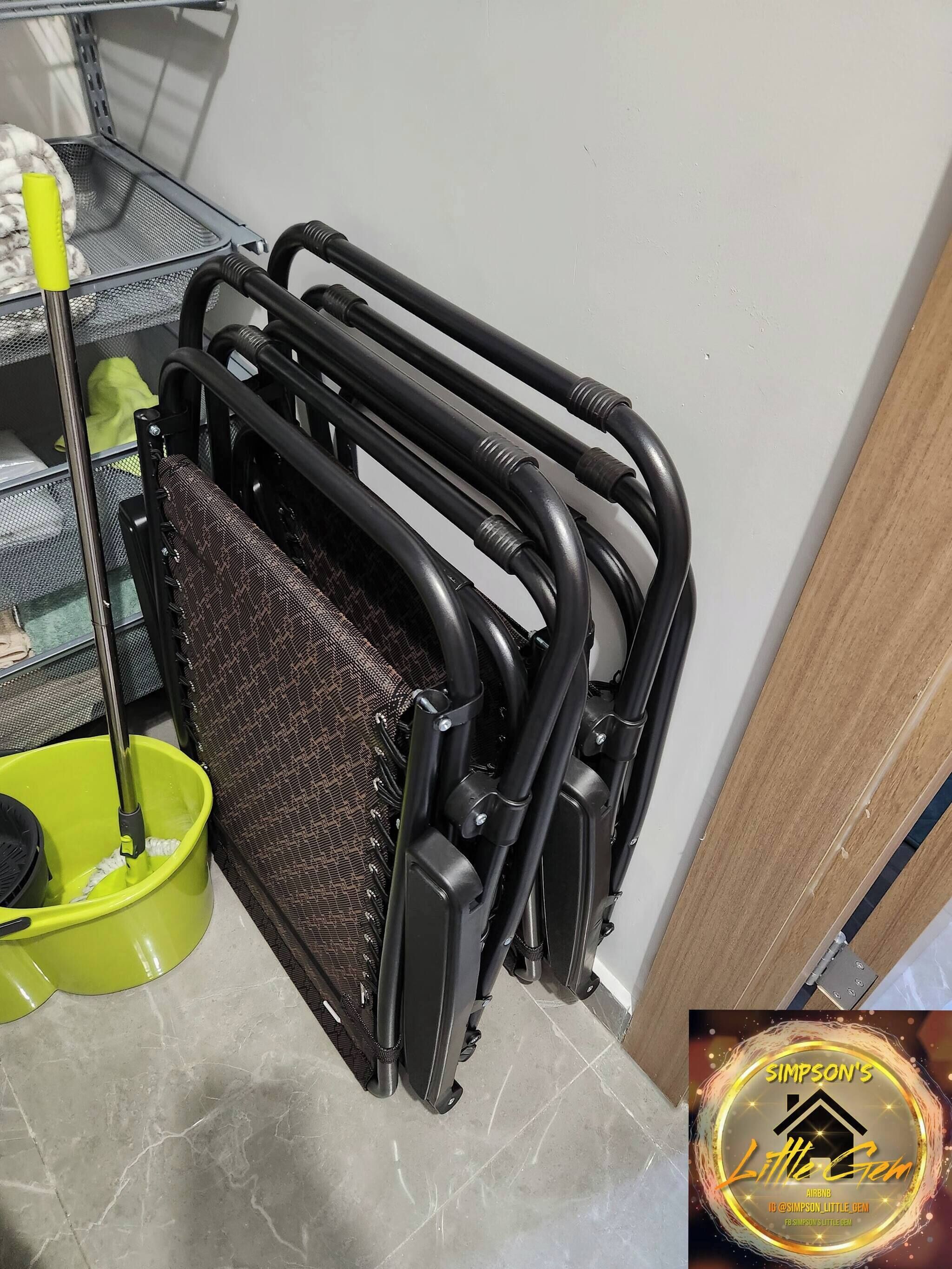 Une pièce dans laquelle on trouve un présentoir métallique servant à ranger un balai et un seau, un panier en osier et une chaise noire.
