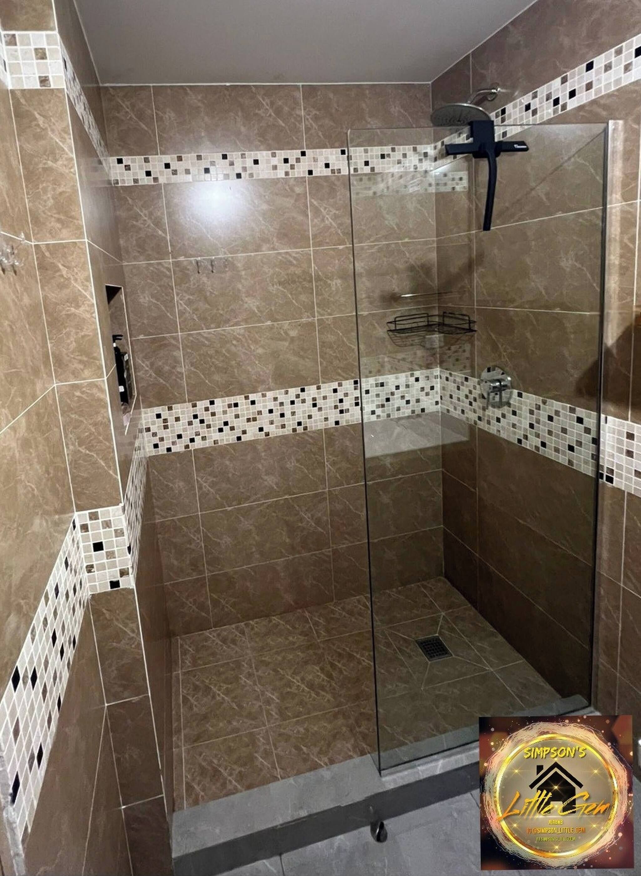 A glass-enclosed shower with a tiled floor and walls, a handheld showerhead, and a small shelf.