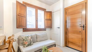 Ein Zimmer mit einer Couch, einem Holzespeisetisch, Stühlen, einem runden Couchtisch mit Pflanze und einer großen Holztür.