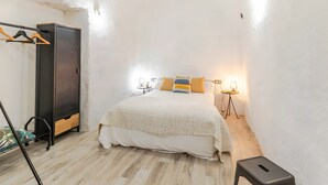 Ein Schlafzimmer mit einem Bett, einem Kleiderschrank, einem kleinen Hocker und einem Tisch mit einer Lampe.