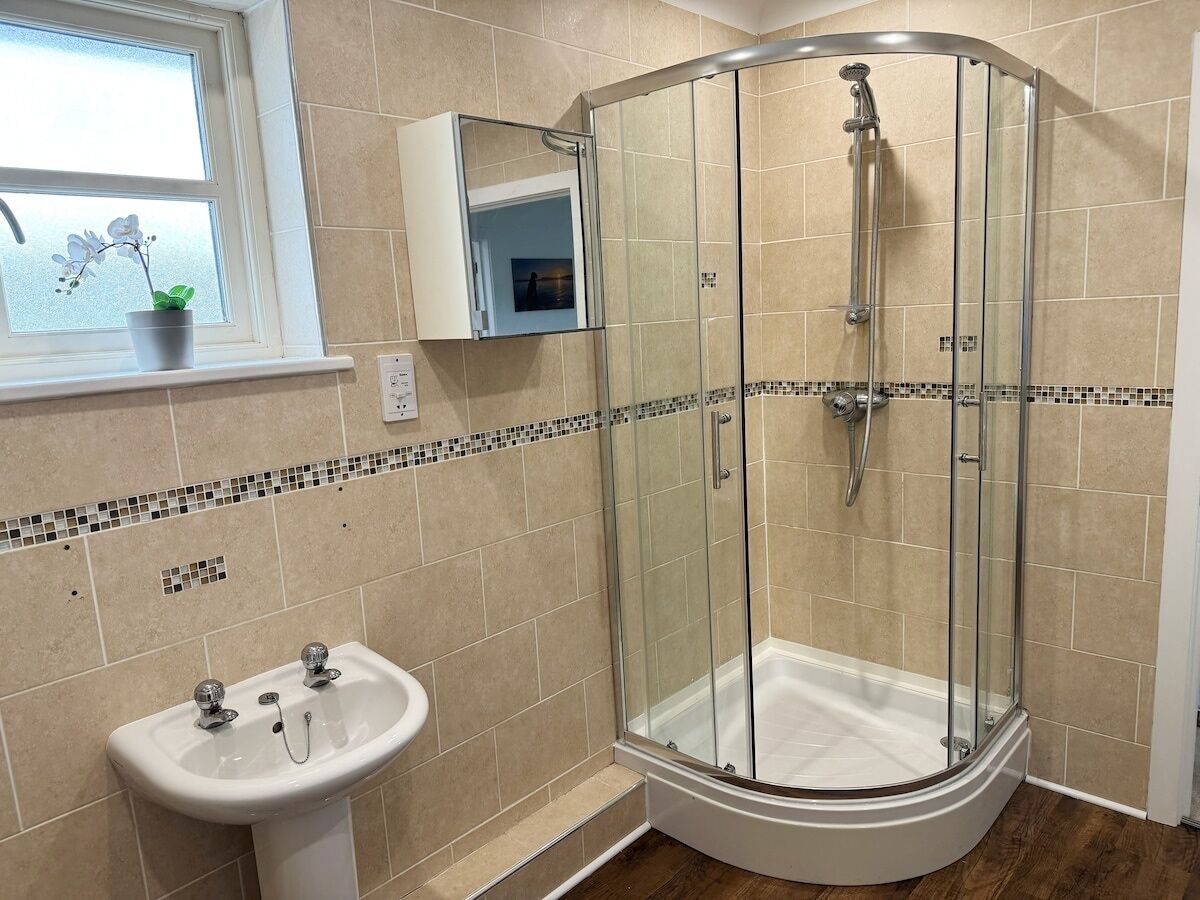 A bathroom with a glass-enclosed shower, a sink, and a window with an orchid plant.