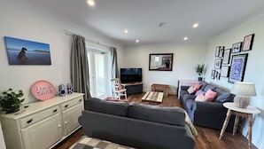 A living room with a sofa, a TV, a coffee table, and a dining table. There is a plant on the left side and a lamp on the right side. - Peg-y-Don : Stunning Holiday Cottage in Newport, Pembrokeshire (Newport)