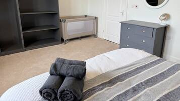 A bedroom with a bed, a grey dresser, a wardrobe, a bench, and a round mirror.