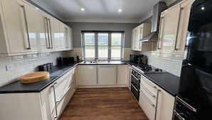 A kitchen with white cabinets, a black countertop, and a wooden floor. - Peg-y-Don : Stunning Holiday Cottage in Newport, Pembrokeshire (Newport)
