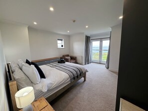 Ein modernes Schlafzimmer mit einem großen Bett, Nachttischen, einem Fenster mit Vorhängen und Blick ins Freie.