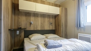 A bedroom with a wooden wall, a bed with white bedding, and a built-in wardrobe above the bed. - Chalet 809 with all comforts on the edge of the forest (La Teste-de-Buch)