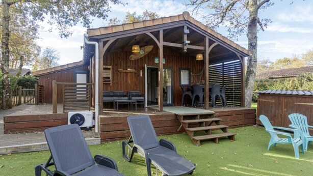 A wooden cabin with a covered porch, outdoor seating, and a small stage. - Chalet 809 with all comforts on the edge of the forest (La Teste-de-Buch)