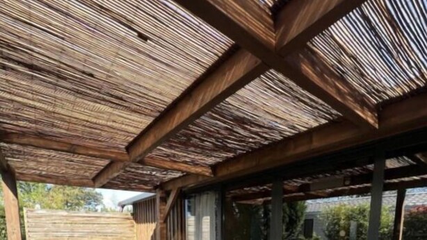 Una terraza de madera al aire libre con mesas de picnic y una estructura de pérgola.