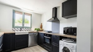 Ett modernt kök med svarta skåp, vitvaror i rostfritt stål, en inbyggd ugn, mikrovågsugn och en tvättmaskin.