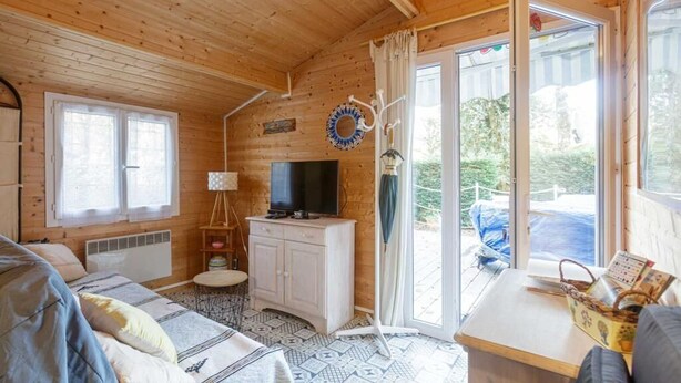 A cozy cabin with a wooden interior, a television on a cabinet, a bed with patterned bedding, and a view through a glass door. - Chalet 213 on the edge of a forest (La Teste De Buch)