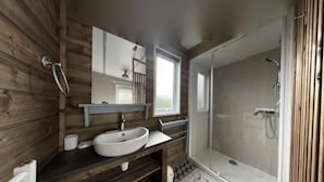 Un baño tipo cabaña de madera con un espejo grande, un lavamanos, una ducha y una ventana.