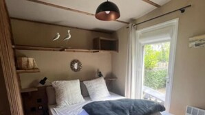 Ein kleines, helles Schlafzimmer mit Bett, Nachttischen, einer Hängelampe und einem Fenster mit Vorhängen.