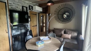 Ein kompakter Wohnraum mit Esstisch, Stühlen, einer Couch, einem Fernseher und einem modernen Deckenventilator.