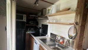 Eine kompakte Küche mit Holzausstattung, einer integrierten Mikrowelle, einem Spülbecken und einem kleinen Kühlschrank.