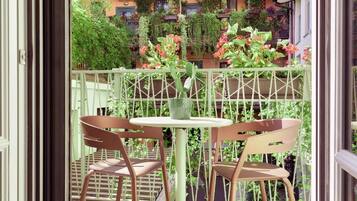 Un balcon agrémenté de deux chaises et d’une table, entouré d’une végétation luxuriante et de plantes suspendues.