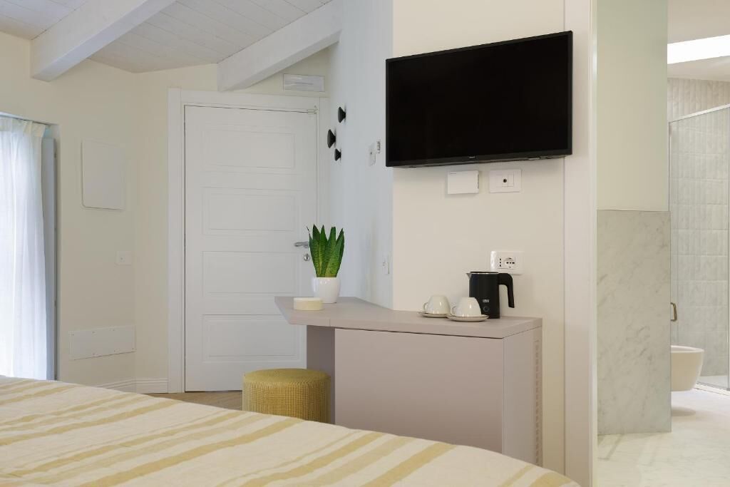 A hotel room with a bed, a small desk with a plant, a television, and a bathroom visible.