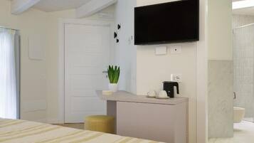 A hotel room with a bed, a small desk with a plant, a television, and a bathroom visible.