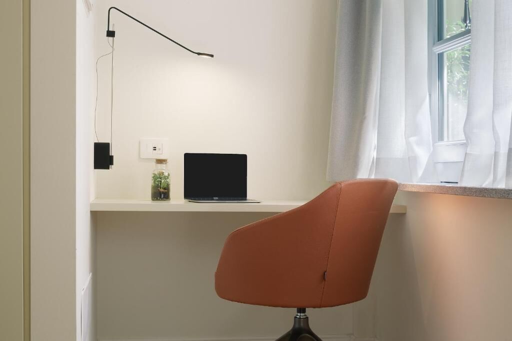 Un'area di lavoro con una scrivania, un portatile, una sedia e una finestra con tende.