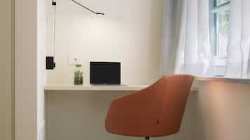 Un'area di lavoro con una scrivania, un portatile, una sedia e una finestra con tende.
