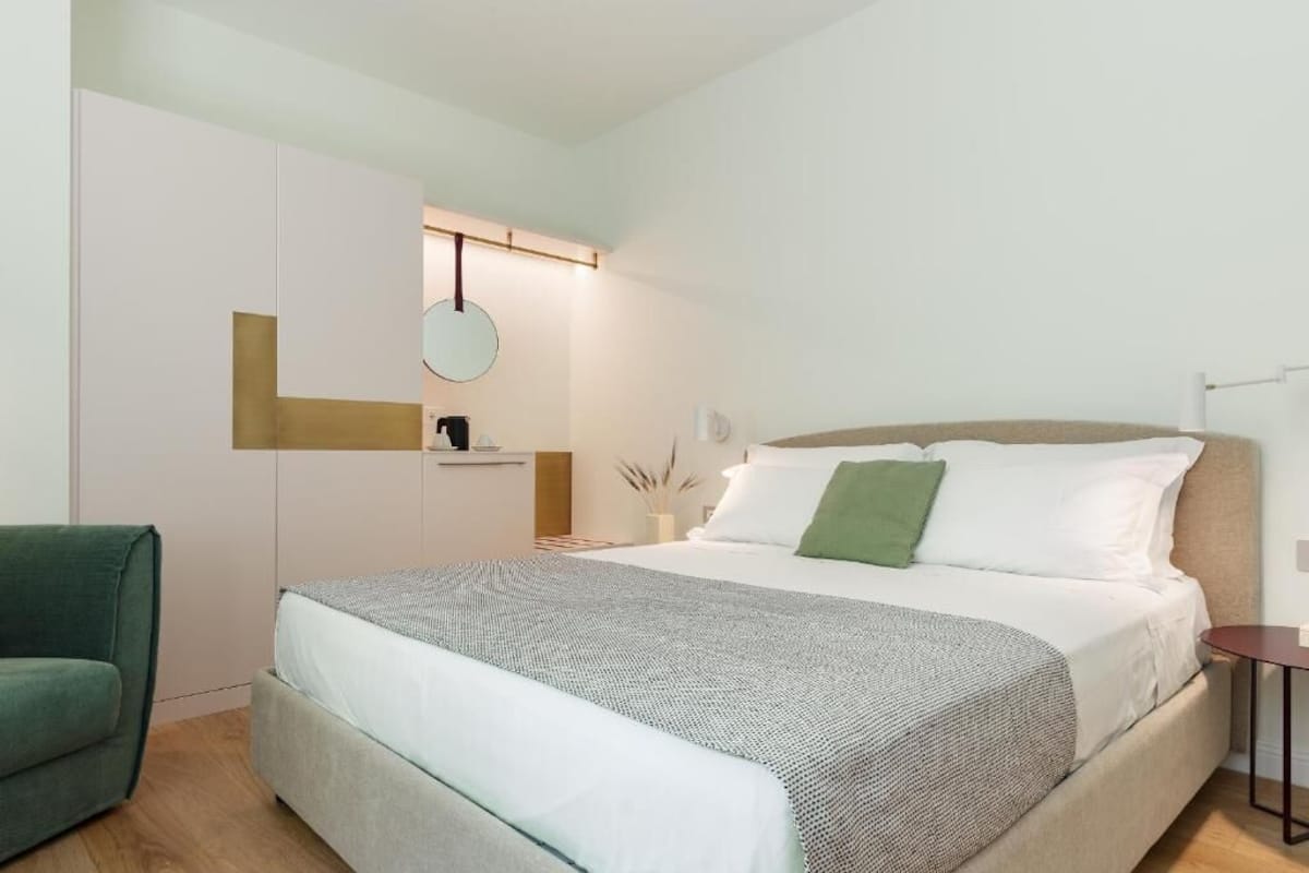 A modern bedroom with a large bed, a green armchair, a bedside table, and a wardrobe.