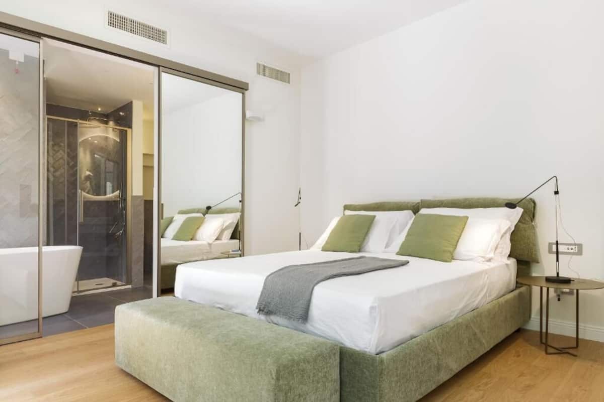 A modern bedroom with a large bed, a glass shower enclosure, and a small bedside table.