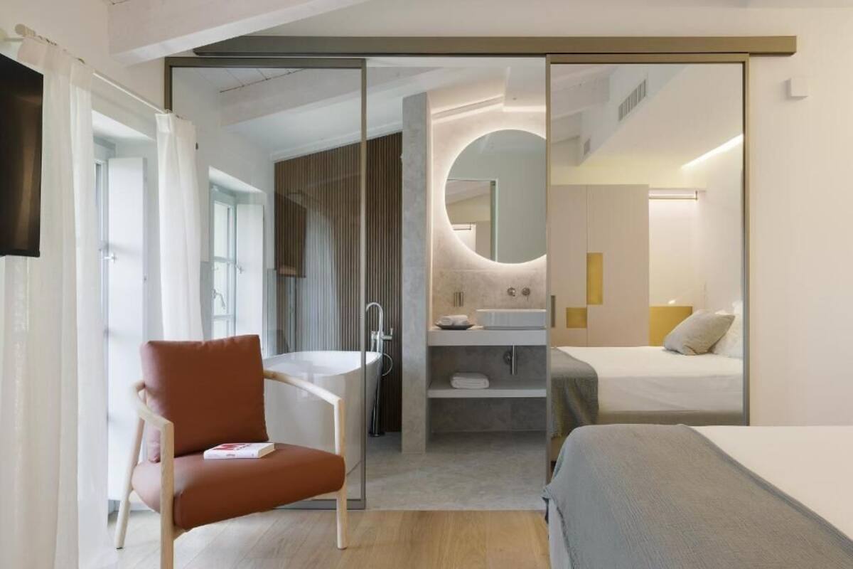 A modern hotel room with a sliding door leading to a bathroom, a single bed, a chair, and a small table with a book.