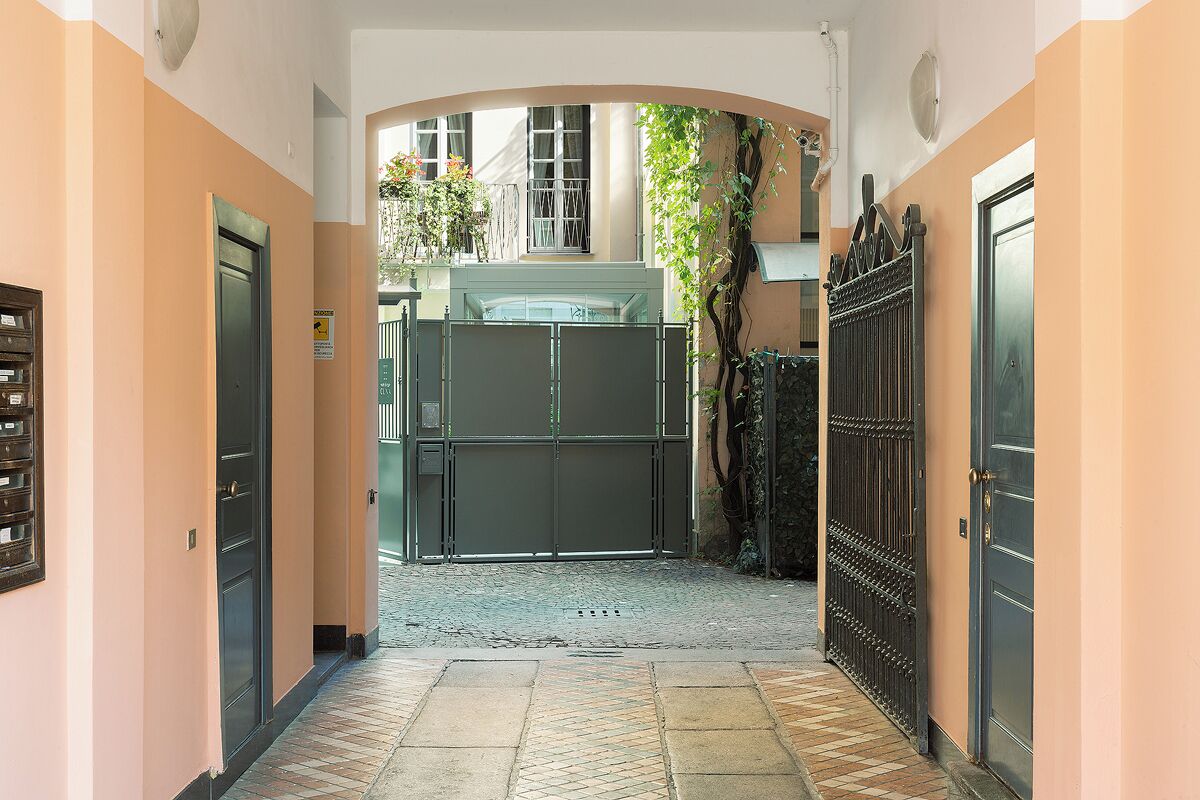 A corridor with a closed gate, a metal fence, and a building entrance.