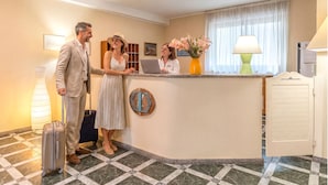 A hotel reception area with a check-in counter, a reception desk, a large window with curtains, and a lamp. - Studio house in a central location in Alghero (Alghero)